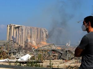 A man wearing a protective mask against the coronavirus stands across the road from the damaged grain silos of Beirut's harbour August 5, 2020, one day after a powerful twin explosion tore through Lebanon's capital, resulting from the ignition of a huge depot of ammonium nitrate at the city's main port. STR / AFP