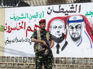 A fighter loyal to Yemen's Huthi rebels stands guard next to a mural denouncing Abu Dhabi Crown Prince Sheikh Mohammed bin Zayed Al Nahyan (R) and Israeli Prime Minister Benjamin Netanyahu, during a rally in the capital Sanaa, on August 22, 2020, to protest the US-brokered deal to normalise Emirati-Israeli relations. MOHAMMED HUWAIS / AFP