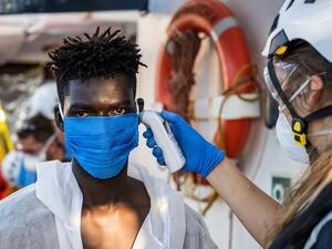A crew member takes the temperature of a migrant  who has just been helped off Banksy's ship who is wearing protective clothes and a face mask (AFP)