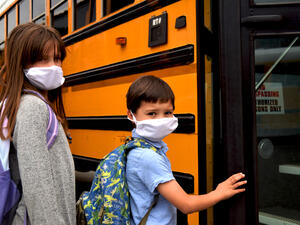 Boy and girl, students, children wearing face masks getting on school bus. (Shutterstock/ File Photo)