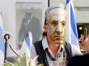 An Israeli comedian, wearing a mask bearing the portrait of Prime Minister Benjamin Netanyahu, smokes a cigar during a fake cabinet meeting to protest the Israeli government's policy and mismanagement of the Covid-19 pandemic in the coastal city of Tel Aviv on September 6, 2020. JACK GUEZ / AFP