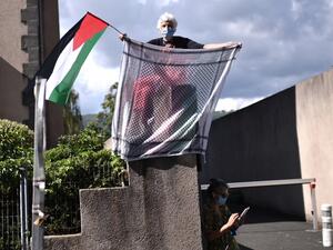 A woman holds a keffiyeh and a Palestinian flag as the pack rides during the 13th stage of the 107th edition of the Tour de France cycling race, 191 km between Chatel-Guyon and Puy Mary, on September 11, 2020. Marco BERTORELLO / AFP