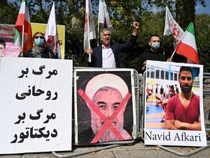 Protesters wave the Lion and Sun flag of the National Council of Resistance of Iran and the white flag of the People's Mujahedin of Iran, two Iranian opposition groups, with a placard depicting the crossed out face of Iran's President Hassan Rouhani as they demonstrate outside the Iranian embassy in London on September 12, 2020 against the execution of Iranian wrestler Navid Afkari in the southern Iranian city of Shiraz and against the Iranian government. Iran said it executed wrestler Navid Afkari, 27, on 