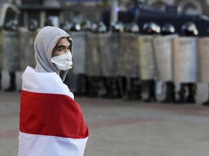 An opposition supporter wrapped in a former white-red-white flag of Belarus stands in front of law enforcement officers blocking the road during a demonstration called by the opposition movement for an end to the regime of authoritarian leader in Minsk on September 20, 2020. Tens of thousands of opposition supporters marched in the Belarusian capital of Minsk defying a heavy security force presence that included water cannons and armoured vehicles. Belarus President Alexander Lukashenko, who has ruled the e