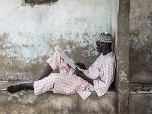 A man reads a newspaper as he waits for the tide to recede in Bargny on September 02, 2020. Fishing villages like Bargny have been fighting the rising seas for decades, hundreds of houses have been lost and families displaced. JOHN WESSELS / AFP