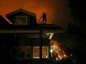 Michael Kunch uses a garden hose to water down his roof as a protective measure as the Bobcat Fire burns down a nearby hillside on September 15, 2020 in Monrovia, California. MARIO TAMA / GETTY IMAGES NORTH AMERICA / Getty Images via AFP