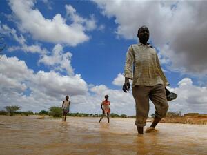 Sudanese people walk in flood water after torrential rain in the town of Osaylat, 50km southeast of Khartoum, on 6 August 2020 (AFP)
