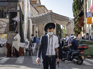An Ultra-orthodox Jewish man clad in face mask and wearing Tefillin or phylacteries (small black leather box containing scrolls of parchment inscribed with verses from the Torah) walks past others praying outdoors in Jerusalem, during the second nationwide lockdown imposed by the government in a bid to stem the increase of COVID-19 coronavirus cases, on October 1, 2020. MENAHEM KAHANA / AFP