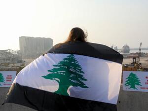 In this file photo taken on September 4, 2020, a woman, draped in a black-striped Lebanese flag, looks at the site of the massive explosion at Beirut's port area, during a demonstration to mark one month since the cataclysmic August 4 explosion that killed 191 people, in the Lebanese capital Beirut. (AFP/File)