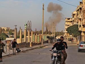 A smoke plume rises following an explosion in the town of Ariha in the rebel-held northwestern Idlib province on October 20, 2020, while a Turkish military convoy drives through after vacating the Morek post in Hama's countryside. Turkey started withdrawing from one of its largest outposts in northwest Syria encircled for the past year by Syrian regime forces, a war monitor and a pro-Ankara rebel commander said. The outpost in Morek is Turkey's largest in the northwest province of Hama, which is now mostly 