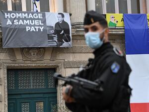 A French police officer stands next to a portrait of French teacher Samuel Paty on display on the facade of the Opera Comedie in Montpellier on October 21, 2020, during a national homage to the teacher who was beheaded for showing cartoons of the Prophet Mohamed in his civics class. France pays tribute on October 21 to a history teacher beheaded for showing cartoons of the Prophet Mohamed in a lesson on free speech, an attack that has shocked the country and prompted a government crackdown on radical Islam.