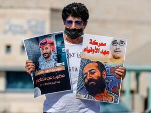 An Israeli left-wing activist lifts posters during a demonstration calling for the release of Palestinian administrative detainees, including Maher al-Akhras, (image L) who's health has deteriorated while on hunger strike, during a protest outside the Israeli run Ayalon prison in Ramle near the coastal city of Tel Aviv, on October 24, 2020. AHMAD GHARABLI / AFP