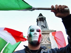 A protestor, wearing a mask in the colors of the Italian flag, holds a flag as he takes part in a protest rally against a new series of restrictions to stop a rise in Covid-19 cases, even as the government considers more stringent measures, in Rome on October 31, 2020. Alberto PIZZOLI / AFP