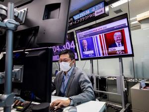 A currency trader works at his desk as a screen shows news updates on the US presidential election featuring portraits of US President Donald Trump (R) and Democratic Party candidate Joe Biden, at a foreign exchange trading company in Tokyo on November 5, 2020. Behrouz MEHRI / AFP