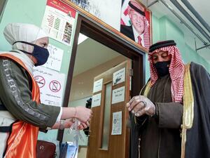 A voter, mask-clad due to the COVID-19 coronavirus pandemic, is assisted by a volunteer to put on a plastic glove before entering a polling station in Jordan's capital Amman on November 10, 2020, during the 2020 general election. AFP