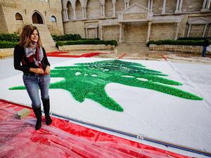 Caroline Chaptini, an environmental activist, poses next to a partially-completed 300-square-metre Lebanese national flag made up from plastic bottles, caps, and empty bullet cartridge set up by activists at an open-air restaurant and wedding venue in the town of Bnachii in northern Lebanon on November 21, 2020, a day ahead of the country's 77th independence day. Ibrahim Chalhoub / AFP