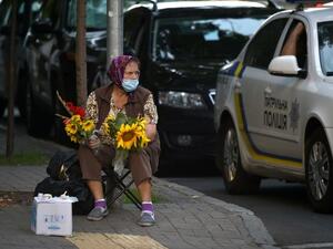 An elderly woman wearing a face mask to protect against the coronavirus disease sells flowers in the center of the Ukrainian capital of Kiev on a hot summer day on July 21, 2020. (AFP)