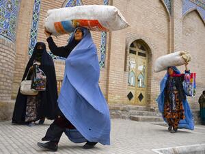 Burqa-clad women carry their belongings as they walk past the Jama Mosque in Herat on December 3, 2020. HOSHANG HASHIMI / AFP
