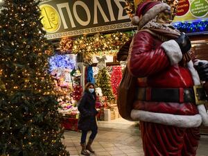A woman wearing a protective face mask walks past a Santa Claus outside a shop selling Christmas decoration, in Athens, on December 7, 2020. ANGELOS TZORTZINIS / AFP