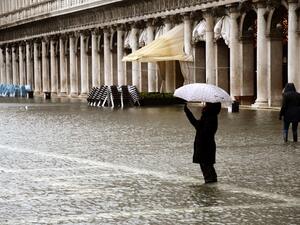 A person takes photos while standing on a flooded St. Mark's Square on December 8, 2020 in Venice following a high tide "Alta Acqua" event following heavy rains and strong winds, and the mobile gates of the MOSE Experimental Electromechanical Module that protects the city of Venice from floods, were not lifted ANDREA PATTARO / AFP