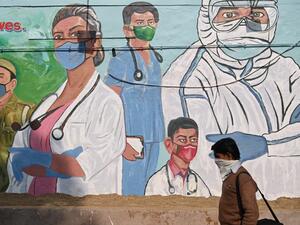 A man walks past a mural depicting Covid-19 coronavirus frontline workers in New Delhi on December 9, 2020. Sajjad HUSSAIN / AFP