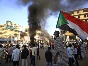 A Sudanese man wearing a face mask waves his country's national flag during protests in the capital Khartoum to mark the second anniversary of the start of a revolt that toppled the previous government, on December 19, 2020. Frustrated by the lack of change in their daily lives, thousands of demonstrators, mostly young, marched in several towns in Sudan. ASHRAF SHAZLY / AFP