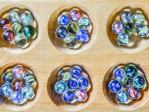Traditional Mancala boardgame with glass pieces on wooden table  (Shutterstock)	