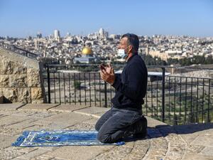 A mask-clad Palestinian, unable to reach the Al-Aqsa mosque compound amidst strengthened restriction due to the coronavirus, perform Friday prayers at the Mount of Olives overlooking the compound in the Old City of Jerusalem on January 8, 2021. AHMAD GHARABLI / AFP