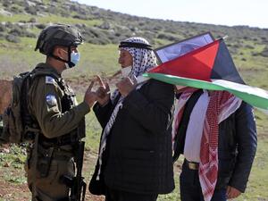A Palestinian protester carrying the national flag confronts Israeli security forces during a demonstration against the expansion of settlements near the village of Beit Dajan, east of Nablus, in the occupied West Bank, on January 8, 2021. JAAFAR ASHTIYEH / AFP