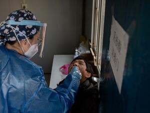 A woman (R) gets a nucleic acid test at a testing booth outside the Red Cross hospital in Wuhan on January 11, 2021, as the city marks the first anniversary of when China confirmed its first death from the COVID-19 coronavirus. NICOLAS ASFOURI / AFP