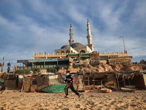 A Palestinian boy wearing a mask for protection against the COVID-19 coronavirus pandemic runs along a beach beneath a mosque in Gaza City on January 27, 2021. MOHAMMED ABED / AFP