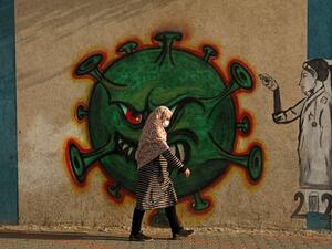 A Palestinian woman, wearing a protective mask amid the COVID-19 pandemic, walks past a coronavirus-inspired mural in Gaza City, on February 2, 2021. Mohammed ABED / AFP