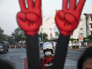 A policeman looks on next to a cut-out of the three finger salute during a demonstration against the military coup in Yangon on February 7, 2021. STR / AFP