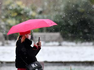 A pedestrian wearing a face mask or covering due to the COVID-19 pandemic, shelters from the snow beneath an umbrella in Green Park in central London on February 9, 2021. Cold weather swept across northern Europe bring snow and ice. JUSTIN TALLIS / AFP