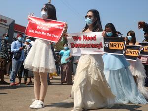 Protesters in gowns hold up signs during a demostration against the military coup in Naypyidaw on February 11, 2021. STR / AFP