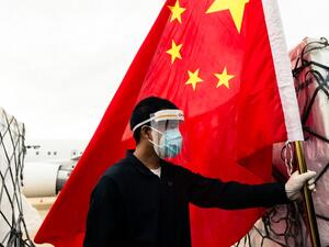 A man wearing a face mask holds the Chinese national flag as he looks on while workers offload an Air Zimbabwe aeroplane with a donation of 200,000 doses of the Sinopharm coronavirus vaccine from China on February 15, 2021 at the Robert Mugabe International Airport. Jekesai NJIKIZANA / AFP