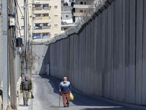 Palestinian men walk by Israel's controversial barrier separating the West Bank city of Abu Dis (background) and East Jerusalem (foreground), on February 16, 2021. AHMAD GHARABLI / AFP