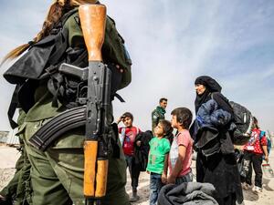 A Kurdish fighter looks on as Syrian women and children, suspected of being related to Islamic State (ISIS) group fighters, gather at the Kurdish-run al-Hol camp, on October 28. (AFP)