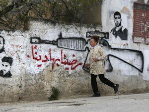 A Palestinian woman walks past a pro-Hamas mural 