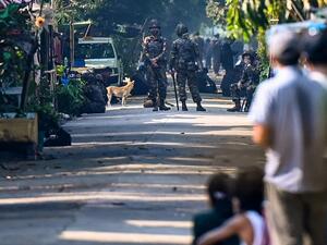 Residents look on as soldiers block a road