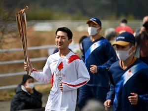 Japanese torchbearer Ryo Matsumoto (L), a student of Nippon Sport Science University, carries an Olympic torch during the first day of Tokyo 2020 Olympic Games torch relay in the town of Naraha, Fukushima Prefecture on March 25, 2021. (Photo: CHARLY TRIBALLEAU / AFP)