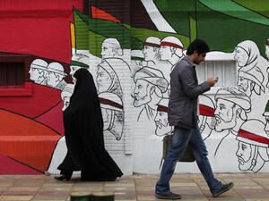 People walk in the Imam Khomeini Street with background street art