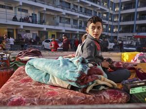 A Palestinian boy who fled his home due to Israeli air and artillery strikes sits on a mattress outside at a school hosting refugees in Gaza city, on May 14, 2021, as cross-border violence between the Israeli military and Palestinian militants continues in the Gaza Strip