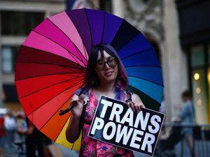 An attendee holds a "Trans Power" sign from under a rainbow umbrella during the annual Dyke March in New York