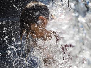 A young boy holds his head under a waterfall at a park in Washington, DC, on June 28, 2021, as a heatwave moves over much of the United States. Swathes of the United States and Canada endured record-setting heat on June 27, 2021, forcing schools and Covid-19 testing centers to close and the postponement of an Olympic athletics qualifying event, with forecasters warning of worse to come. The village of Lytton in British Columbia broke the record for Canada