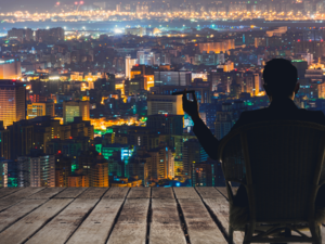Silhouette of businessman sit on chair and hold a cigar and looking at the city in night