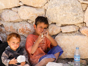 Yong boy playing bamboo flute with his younger brother at the roadside of Roman ruins in Jerash, Jordan