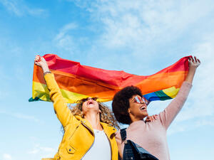Two women friends hanging out in the city waving LGBT with pride flag