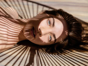 Portrait of beautiful woman with shadows of palm leaf on her face. Concept of sunbathing, vacation.
