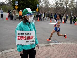 This file photo taken on May 5, 2021 shows a volunteer (L) holding a placard asking people to refrain from watching the competition to prevent the spread of the Covid-19 coronavirus while an athlete (R) competes in the half-marathon race which doubles as a test event for the 2020 Tokyo Olympics, in Sapporo. The public will be asked not to line the route of the Olympic marathon over fears that crowds of fans could spread coronavirus infections, Tokyo 2020 organisers said 
